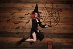 万圣节女巫概念快乐万圣节红色的头发女巫持有魔法飞天扫帚飞行手势木工作室背景