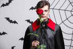吸血鬼万圣节概念肖像英俊的高加索人吸血鬼持有红色的美丽的玫瑰
