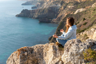 女人<strong>旅游</strong>享受日落海山景观坐在在<strong>户外</strong>岩石海穿牛仔裤蓝色的连帽衫健康的生活方式和谐冥想