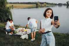 十几岁的高加索人女孩使自拍智能手机家庭背景野餐湖在户外