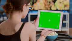 特写镜头年轻的女人持有数字平板电脑绿色屏幕看网络研讨会坐着沙发
