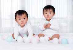 快乐的双胞胎婴儿玩颜色球床上
