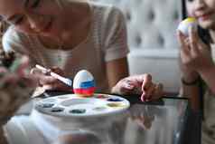 年轻的女人手持有画笔绘画蛋准备复活节节日女儿