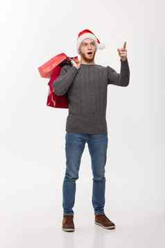 圣诞节概念有吸引力的年轻的高加索人男人。令人惊讶的令人震惊的持有购物袋指出手指前面