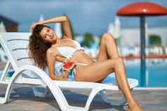 华丽的女模型片西瓜摆姿势在游泳池边阳光明媚的一天