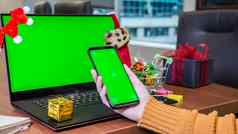 特写镜头女人手持有智能手机绿色屏幕移动PC空绿色屏幕圣诞节装饰礼物盒子背景假期概念在线购物办公室模型