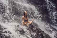 健康水疗中心假期瑜伽冥想概念年轻的女人坐着莲花位置岩石热带瀑布