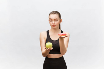 年轻的女人选择甜甜圈苹果白色背景饮食食物概念