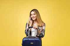 肖像快乐亚洲女旅行者手提箱手机孤立的黄色的背景