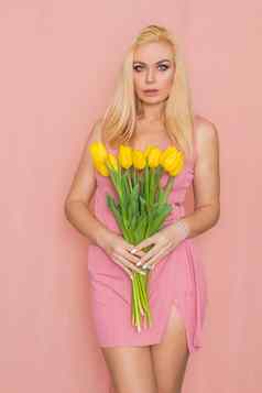 金发女郎粉红色的夏天衣服持有花束黄色的郁金香