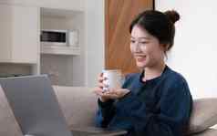 肖像美丽的年轻的亚洲女人工作移动PC在线互联网持有杯坐着沙发首页免费的空间