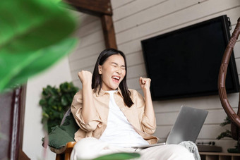 快乐的亚洲女人赢得在线移动PC庆祝胜利大喊大叫欢乐并
