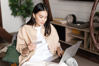 肖像亚洲年轻的女人坐着首页购买移动PC持有信贷卡购物在线