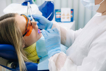 年轻的美丽的女孩牙科眼镜对待牙齿牙医紫外线光填充牙齿