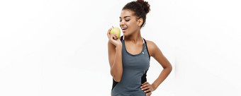 健康的健身概念美丽的美国非洲夫人<strong>灰色</strong>健身衣服吃绿色<strong>苹果</strong>孤立的白色背景