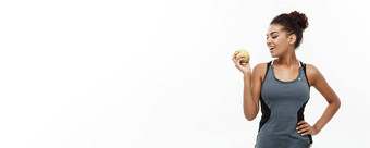健康的健身概念美丽的美国非洲夫人灰色健身衣服持有绿色苹果孤立的白色背景