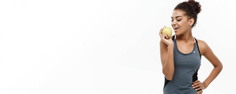 健康的健身概念美丽的美国非洲夫人灰色健身衣服吃绿色苹果孤立的白色背景