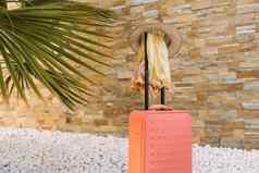 行李前面石头墙白色石头地板上文本橙色手提箱他太阳镜纱笼