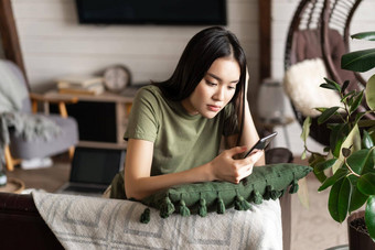 亚洲女孩首页移动电话年轻的漂亮的女人t恤铺设沙发上智能手机