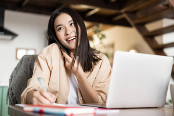 年轻的专业亚洲女人工作首页回答电话调用会说话的客户端写作信息采取笔记谈话坐着移动PC