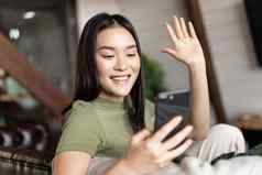 年轻的亚洲女人视频调用移动电话挥舞着手智能手机相机聊天手机首页