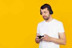 年轻的男人。胡子白色t恤玩家玩视频游戏耳机微笑相机站孤立的黄色的背景