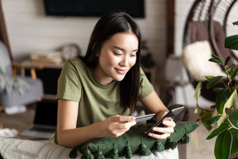 在线购物朝鲜文女孩使购买在线购物应用程序移动电话信贷卡信息支付坐着首页生活房间