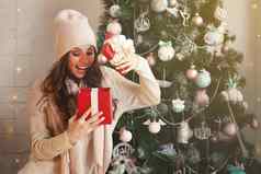 微笑快乐美丽的年轻的女人冬天衣服红色的圣诞节礼物盒子背景装饰圣诞节树女孩高兴地打开礼物问候一年
