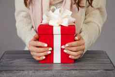 女手持有红色的礼物盒子白色丝带圣诞节礼物盒子灰色的背景女孩持有圣诞节购物问候一年购物出售概念