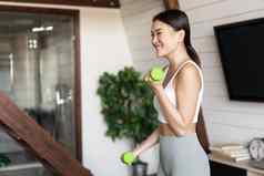 活跃的健康的亚洲女孩适合身体健身练习首页提升哑铃微笑锻炼生活房间