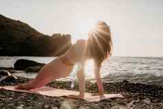中间岁的女人黑色的头发普拉提环瑜伽席海卵石海滩女健身瑜伽概念健康的生活方式和谐冥想