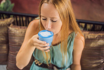 年轻的女人地中海早餐坐着沙发饮料时尚的喝蓝色的拿铁热蝴蝶(2008年)拿铁蓝色的螺旋藻拿铁