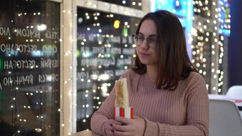 年轻的女人眼镜吃玉米煎饼餐厅女孩坐在咖啡馆晚上窗口装饰花环