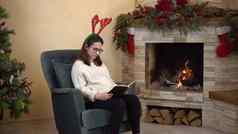 年轻的怀孕了女人眼镜坐在扶手椅壁炉角头读取书圣诞节情绪