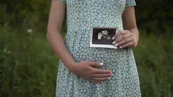 年轻的怀孕了女人持有超声波<strong>图片婴儿</strong>手女孩衣服在户外
