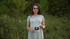 年轻的怀孕了女人持有超声波图片婴儿手女孩眼镜衣服自然