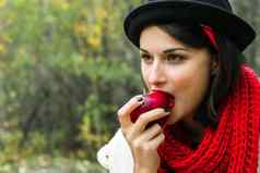 美丽的女人吃成熟的红色的苹果用钩针编织红色的围巾黑色的他户外野餐