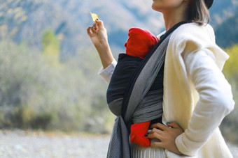 美丽的年轻的妈妈。婴儿婴儿吊索户外妈妈。携带孩子旅行秋天山婴儿袋概念