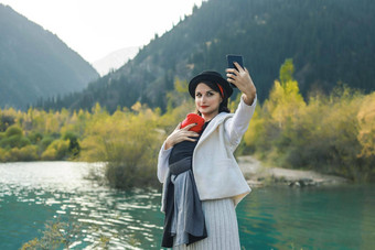 美丽的年轻的妈妈。婴儿婴儿吊索使自拍妈妈。携带孩子旅行秋天山湖活跃的妈妈。概念