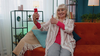 快乐高级祖母持有智能手机看移动视频调用在线使自拍首页