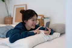 美丽的亚洲女人铺设白色床上移动电话微笑早....周日