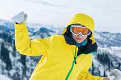 美丽的尤格风女人旅游黄色的夹克滑雪眼镜面具白色连指手套背景山相机冬天假期消遣概念