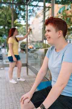 年轻的女孩坐着等待公共汽车站大城市女人在户外公共汽车停止等待有轨电车垂直
