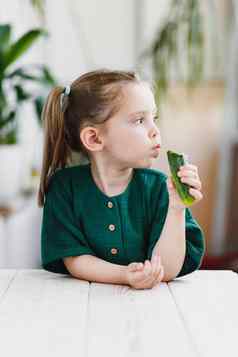 可爱的女孩绿色棉布衣服吃黄瓜新鲜的蔬菜健康的食物概念室内肖像