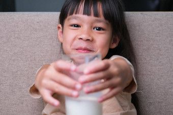 肖像可爱的亚洲女孩持有玻璃牛奶坐着沙发<strong>首页</strong>小女孩<strong>首页</strong>微笑脸感觉快乐享受喝牛奶相机