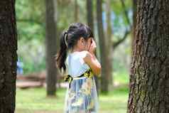 微笑女孩覆盖眼睛手玩隐藏寻求站大树可爱的女孩有趣的在户外公园