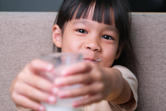 肖像可爱的亚洲女孩持有玻璃牛奶坐着沙发首页小女孩首页微笑脸感觉快乐享受喝牛奶相机