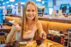 年轻的女人吃寿司咖啡馆