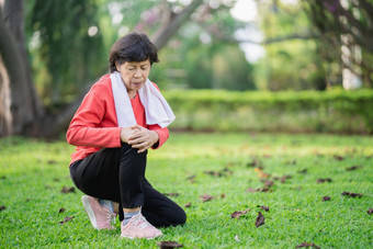 高级亚洲女人膝盖脚踝疼痛运行公园高级亚洲女人坐着地面持有痛苦的膝盖