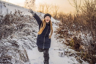 冬天女孩扔雪球相机微笑快乐有趣的在户外下雪冬天一天玩雪可爱的好玩的年轻的女人户外享受雪